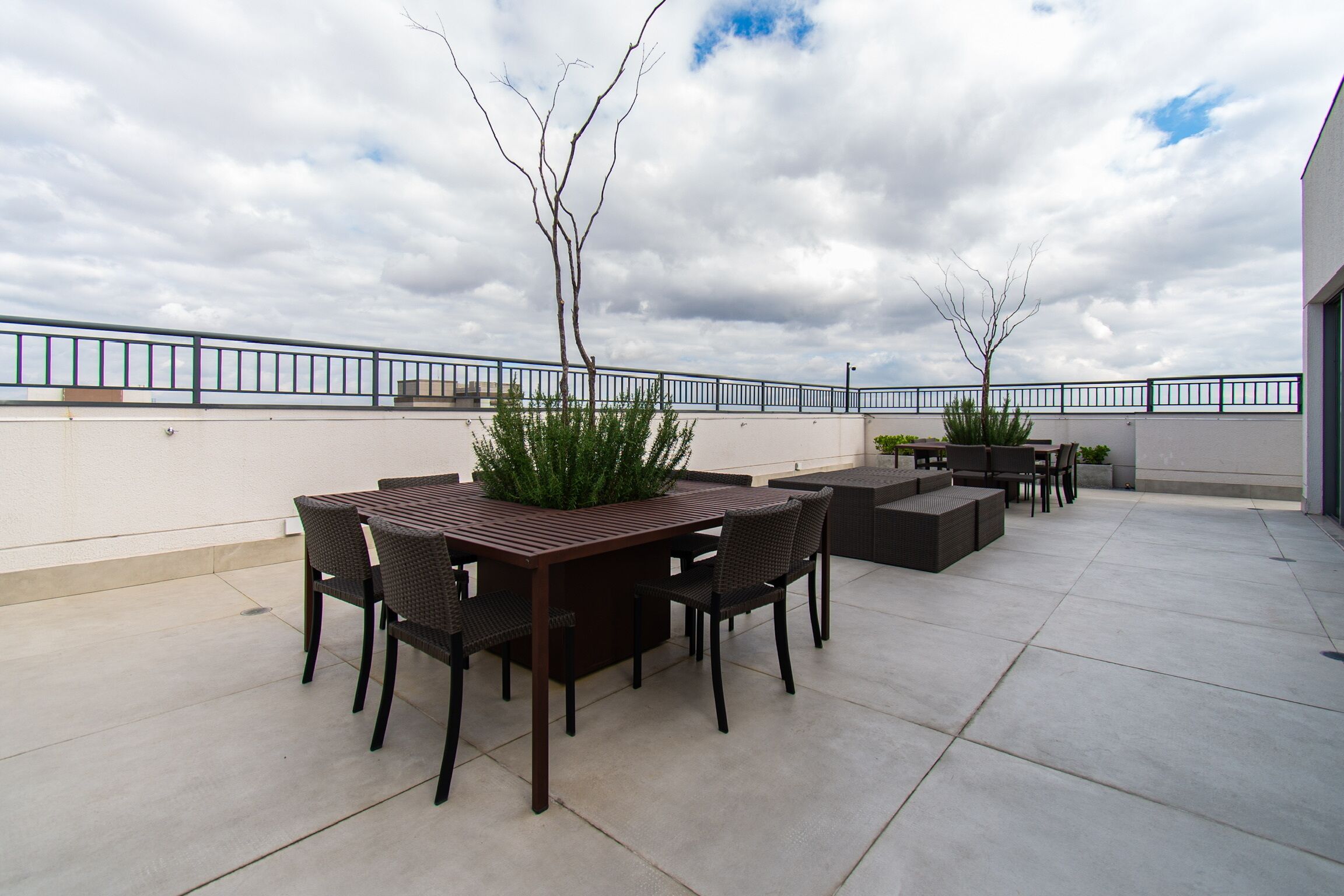 Une terrasse extérieure avec une table et des chaises, entourée de jardinières et d’une rambarde.