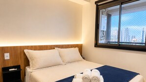 A hotel room with a bed, a nightstand, a window with a city view, and a ceiling light. - Pause Living - Nex One Paraíso (São Paulo)