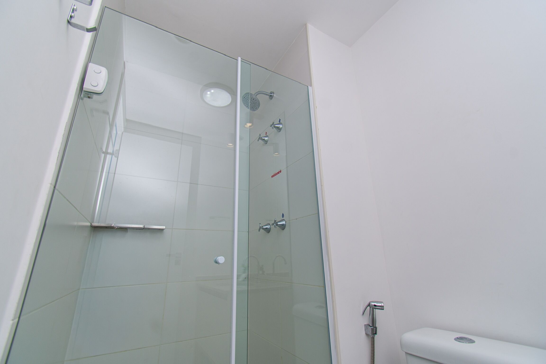 A glass-enclosed shower stall with a handheld showerhead, a handheld faucet, and a wall-mounted faucet.