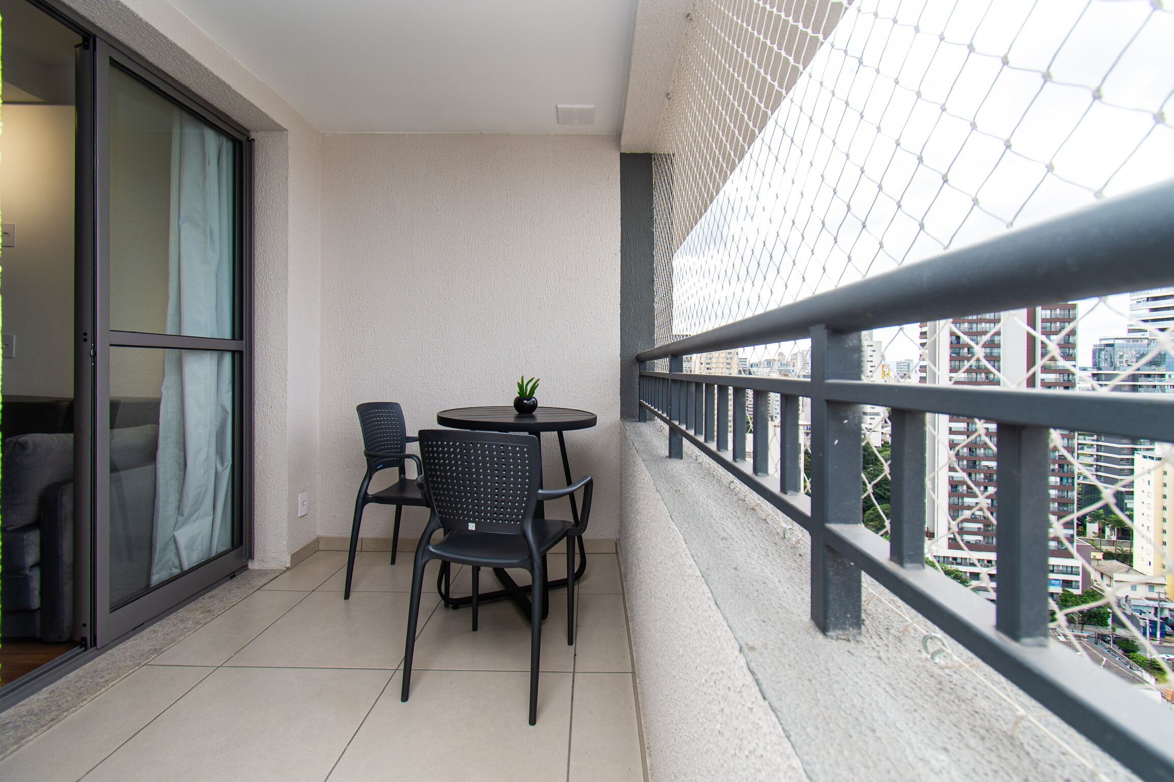 A balcony with a table and chairs, a potted plant, and a view of the cityscape.