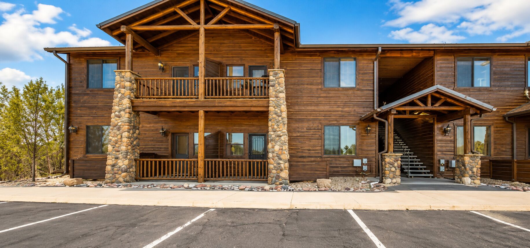 A two-story log cabin with a balcony, stone pillars, and a covered entrance.