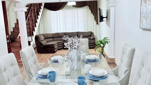 Un coin repas avec une table en verre, des chaises à revêtement blanc et un lustre.