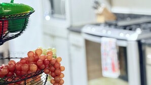 Une cuisine avec des meubles blancs, un fourneau et un panier de fruits contenant des raisins.