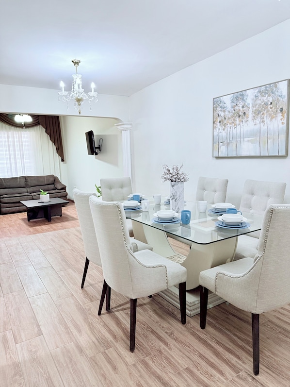 A modern dining area with a glass table, white upholstered chairs, and a chandelier.