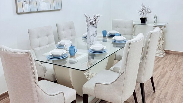 Un coin repas avec une table en verre, des chaises à revêtement blanc, un lustre et un tableau encadré accroché au mur.