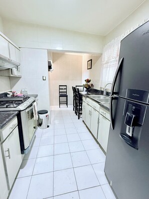 Cuina amb armaris blancs, un refrigerador negre, una cuina i un rentaplat.