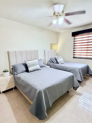 A bedroom with two beds, a ceiling fan, a nightstand, and a window with blinds.