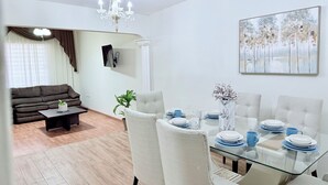 Un coin repas avec une table en verre, des chaises blanches et un lustre.