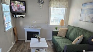 Un salon avec une télévision, une cheminée, un canapé vert et une table basse blanche.