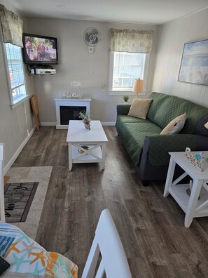 Ein Wohnzimmer mit Fernseher, Kamin, einem grünen Sofa und einem weißen Couchtisch.
