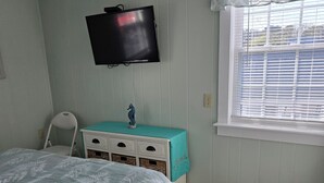 Une chambre à coucher comprenant un lit, une commode, un téléviseur fixé au mur et une fenêtre avec des stores.