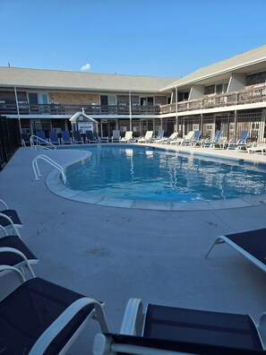 Une piscine avec des chaises longues, un espace de détente couvert et un bâtiment doté de plusieurs balcons.