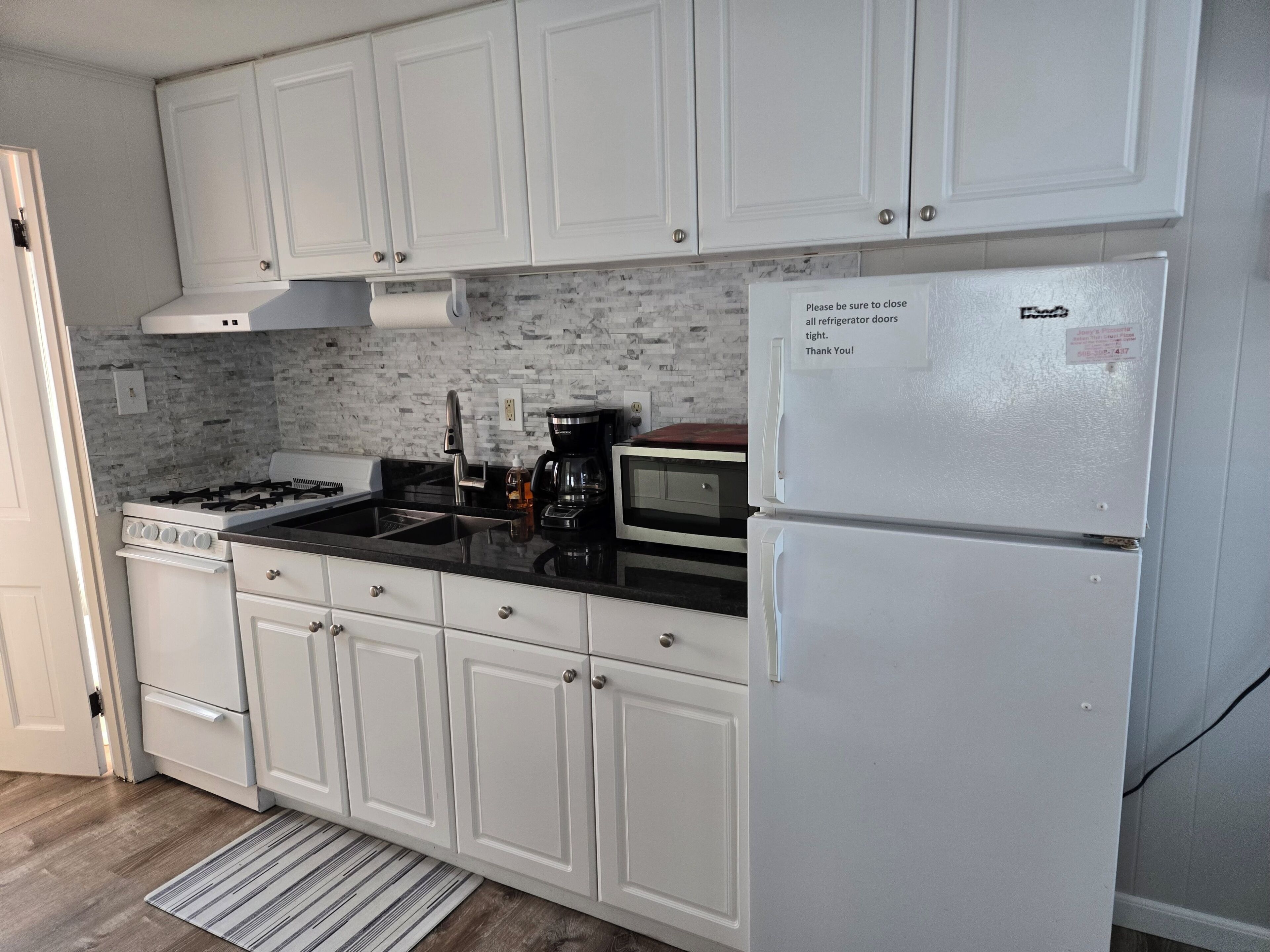 Una cocina con armarios blancos, estufa a gas, microondas y refrigerador.