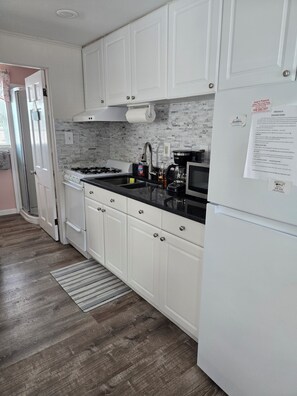 A kitchen with white cabinets, a black countertop, a stainless steel sink, a stove, and a refrigerator.