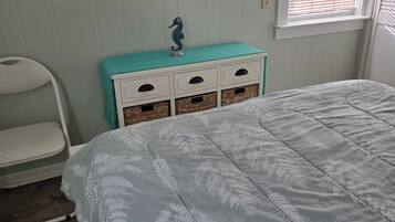 A bedroom with a bed, a dresser with drawers, a chair, a television mounted on the wall, and a window with blinds.