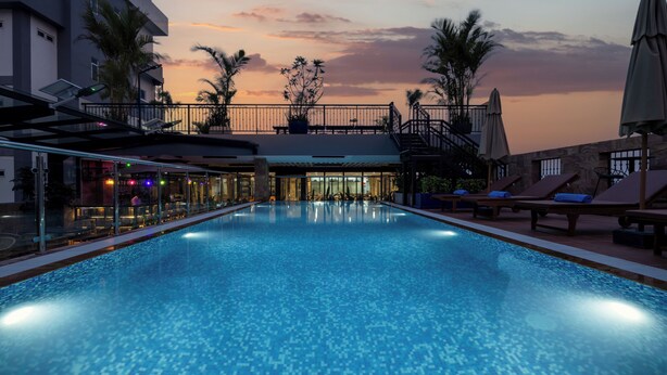 A swimming pool with lounge chairs and a bar area, surrounded by palm trees and a sunset view. - Amana Hotel Phnom Penh (Phnom Penh)