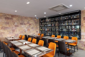 Un restaurante con varias mesas y sillas, una pared de piedra y una zona de bar con estantes llenos de botellas.
