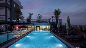 A rooftop pool with a bar area, lounge chairs, and palm trees. - Amana Hotel Phnom Penh (Phnom Penh)