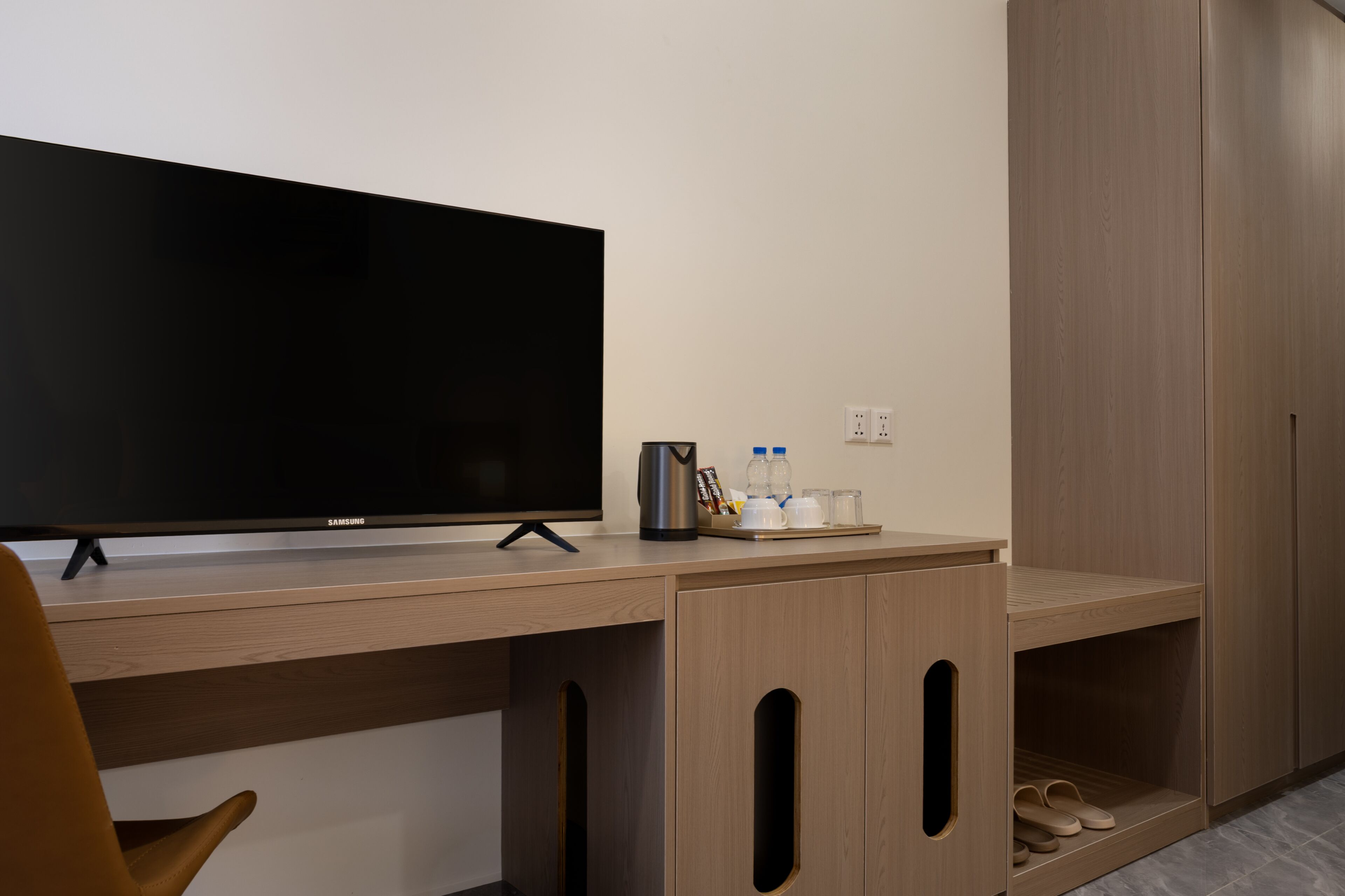 A modern hotel room with a flat-screen TV, wooden desk, and built-in wardrobe.