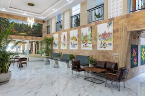 A spacious lobby with a high ceiling, marble flooring, and a seating area with leather sofas and chairs.