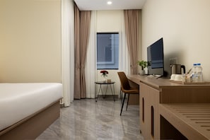 Habitación de hotel con cama, escritorio con televisor, silla, mesita con un florero y ventana con cortinas.