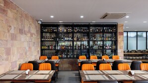 A restaurant with a bar area, multiple tables with orange chairs, and a wall of liquor bottles. - Amana Hotel Phnom Penh (Phnom Penh)
