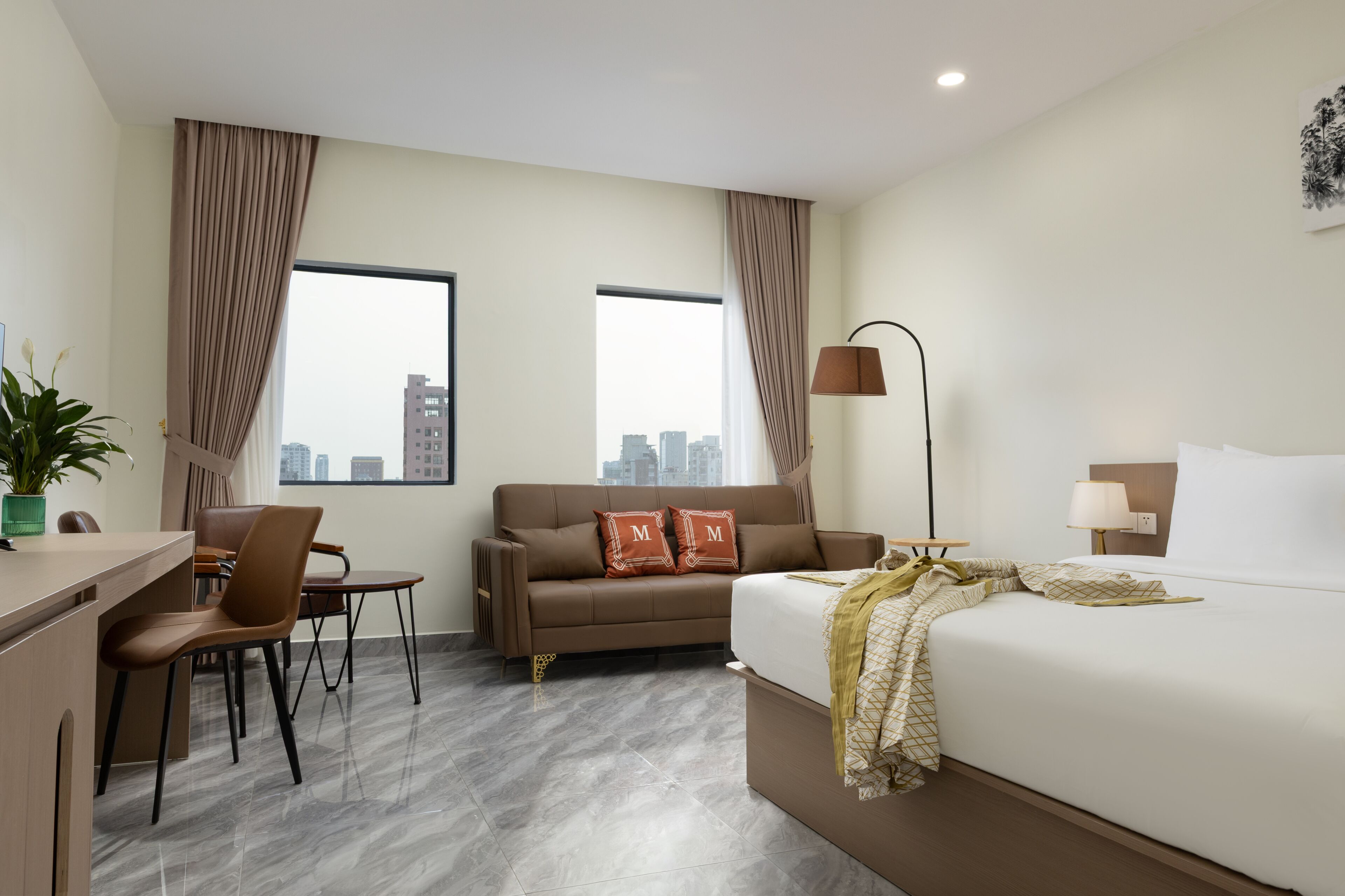 A hotel room with a bed, a desk, a chair, a sofa, and a view of the city.