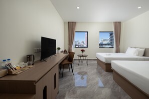 Habitación de hotel con escritorio, televisión, dos camas, una mesita con un florero y vista a la ciudad.