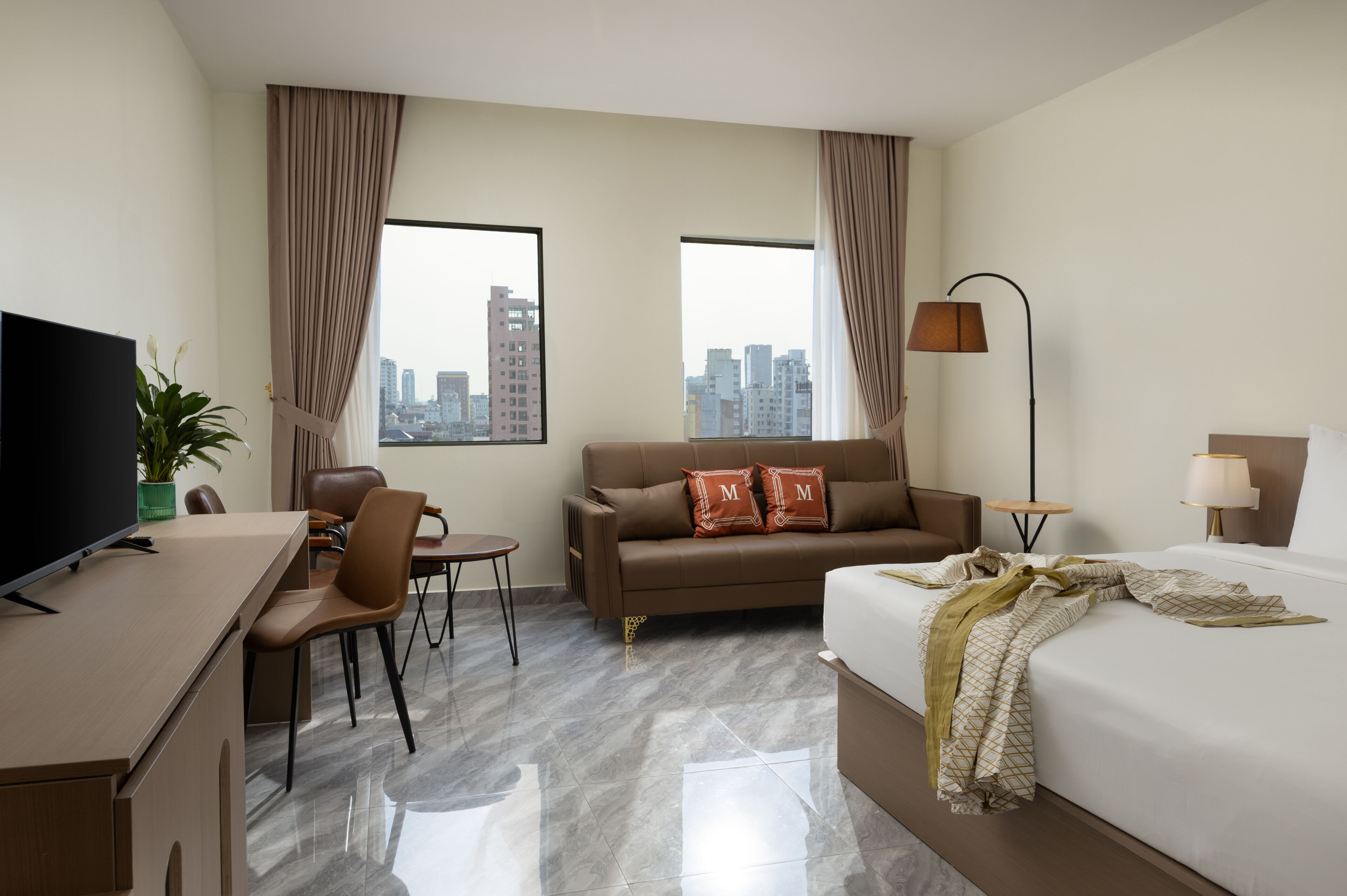 Habitació d'hotel amb llit, escriptori, cadira, sofà, televisió, làmpada i vista a la ciutat.