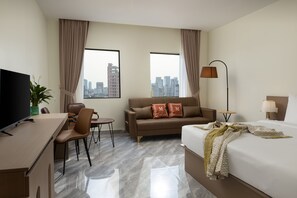Quarto de hotel com cama, escrivaninha, cadeira, sofá, televisão, luminária e vista para a cidade.