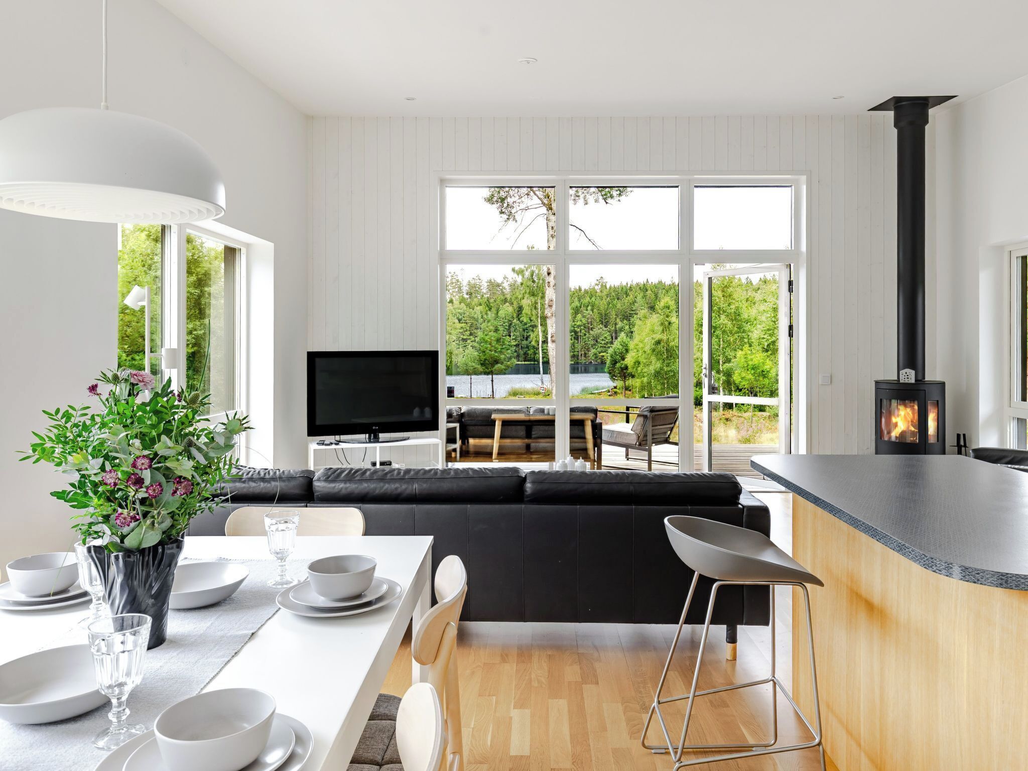 Ett modernt kök med matplats, en svart soffa, en tv och en öppen spis.