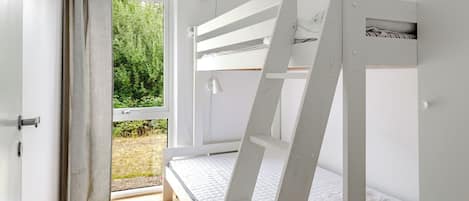 A bedroom with bunk beds, a window with curtains, a white door, and a view of greenery outside.