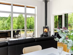 A modern interior with a black wood-burning stove, a black leather sofa, and a dining table with a glass of water. - Paradiset 2 by Interhome (Holmsjö)