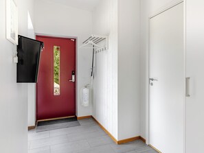 Ein Flur mit einer roten Tür, einer weißen Wand, einer weißen Tür und einem an der Wand befestigten Feuerlöscher.