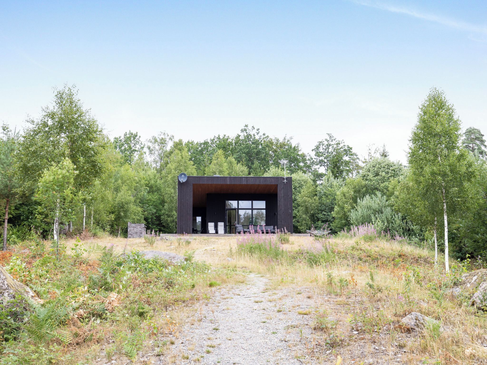 A modern building with a dark exterior, large windows, and a gravel path leading to it.