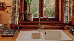 A kitchen with a wooden countertop, a sink, a potted plant, and a window with curtains.