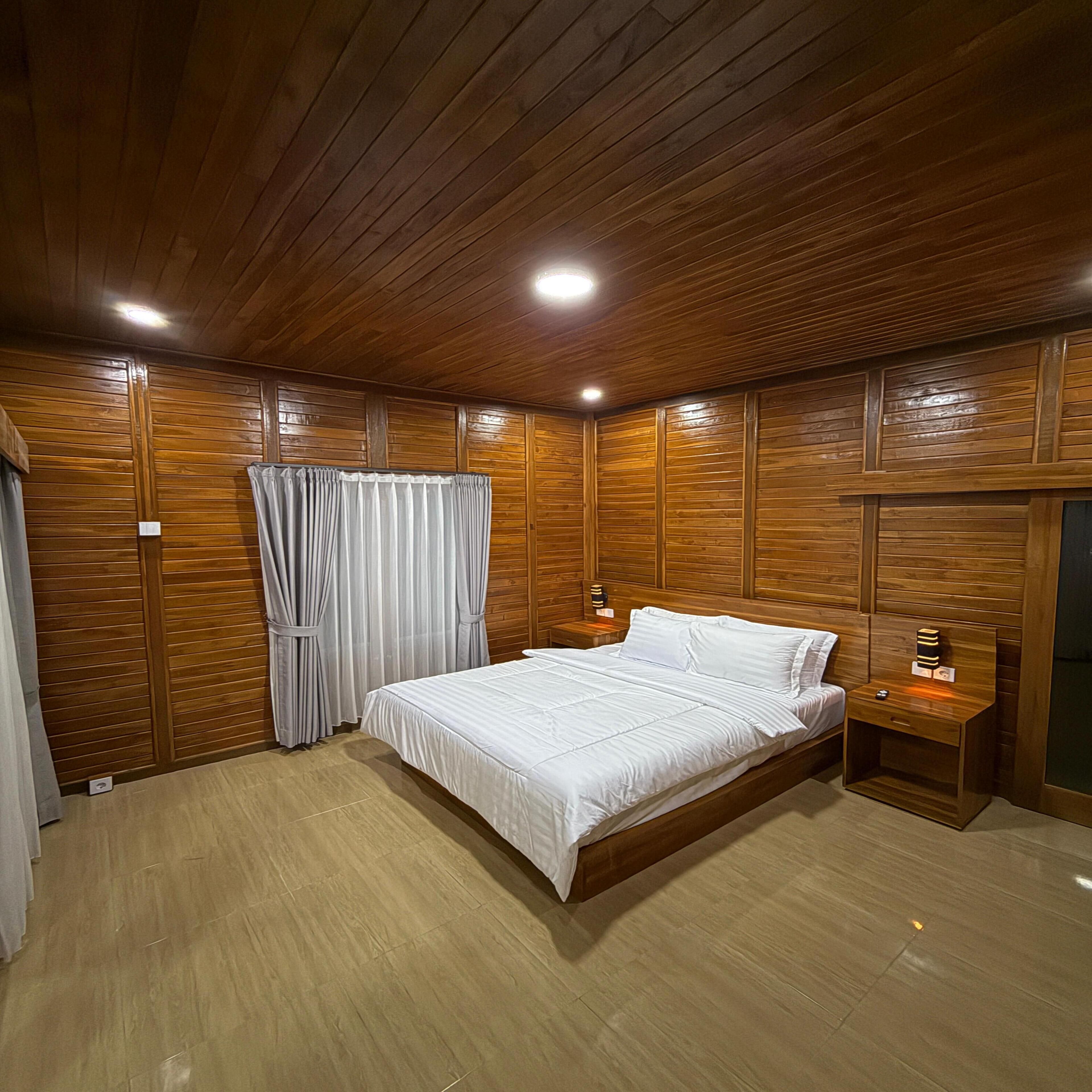 A wooden-paneled bedroom with a bed, curtains, and bedside tables.