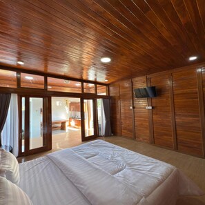 A bedroom with a wooden ceiling, a bed, a TV mounted on the wall, and a sliding glass door leading to a balcony.