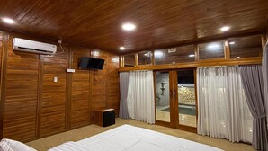 Un dormitorio con techo de madera, una cama, un equipo de aire acondicionado, un televisor y un ventanal corredero que da a una zona de piscina.