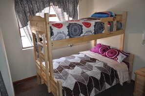 Un lit superposé avec une échelle, une fenêtre avec des rideaux et une table de chevet.