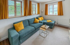 Ein Wohnzimmer mit einer Eckcouch, einem kleinen Tisch und einem Fenster mit Vorhängen.