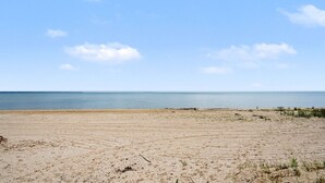 A beach with sand, sparse vegetation, and a calm sea under a clear sky. - Granny`s Cabin on Sandy Lake Huron (Au Gres)