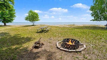 En campingplats med en eldstad, ett picknickbord och utsikt över vattnet.