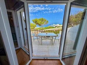 A glass door leading to an outdoor patio with a table and chairs, a view of the sea, and a tree. - Suite with pool and sea views in Cala Morell (Cala'N Morell)
