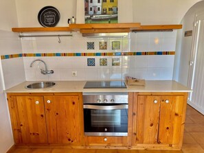 A compact kitchen with wooden cabinets, a built-in oven, a stainless steel sink, and a coffee-themed wall decoration. - Suite with pool and sea views in Cala Morell (Cala'N Morell)