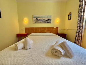 A hotel room with a bed, two nightstands, a painting on the wall, and a patterned curtain. - Suite with pool and sea views in Cala Morell (Cala'N Morell)