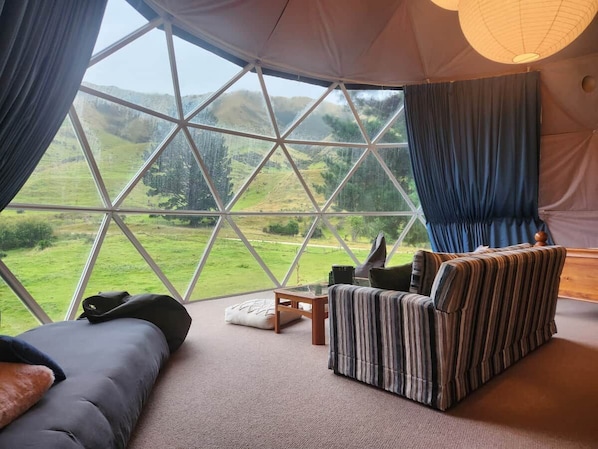 Une pièce confortable avec une grande fenêtre, un lit, un fauteuil à rayures et une petite table.