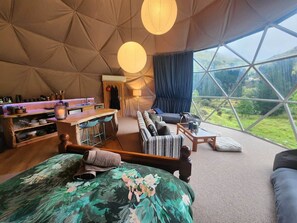 A tent-style room with a bed, seating area, bar, and large windows.