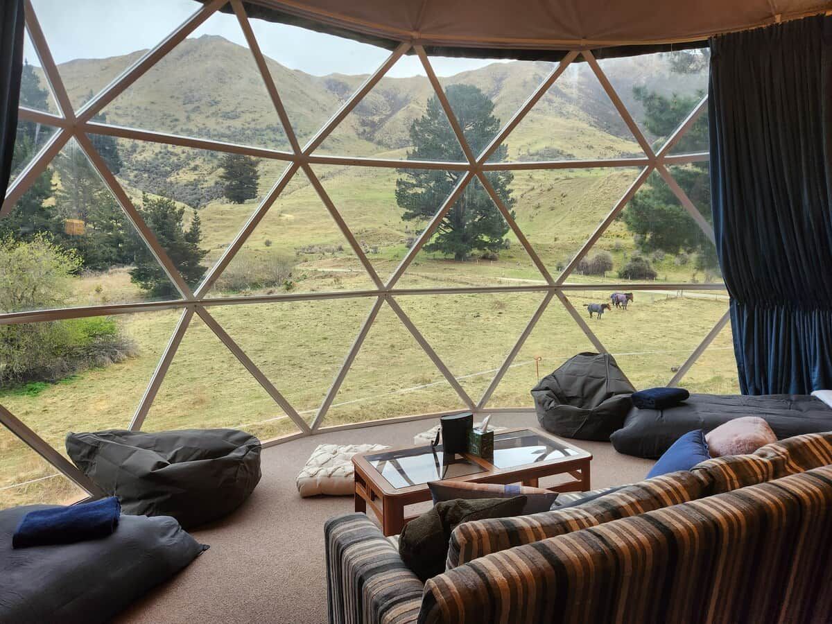 Une pièce dotée d’une grande fenêtre donnant sur un paysage montagneux. On y trouve un canapé, une petite table et un fauteuil en forme de poire.