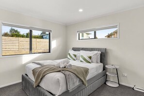 Un dormitorio con cama, mesita de noche, ventana y espejo.